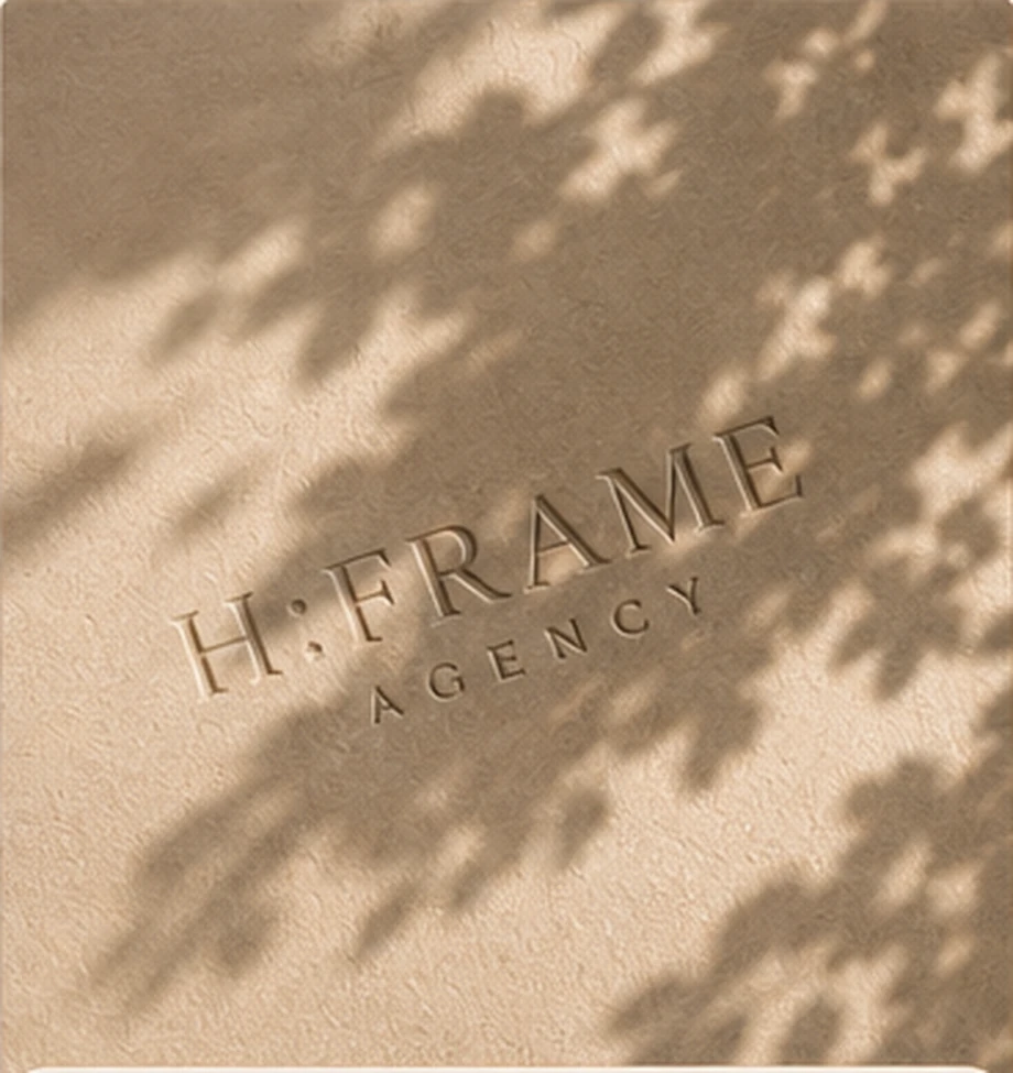 H:FRAME Agency lettering impressed into a warm textured surface beneath natural leaf shadows.